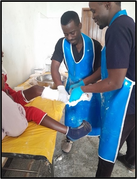 Atención médica y fisioterapia a un niño con discapacidad en Uganda, con personal usando delantales protectores.