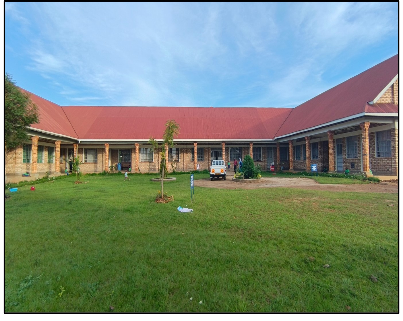 Instalaciones del centro St. Vincent Pallotti en Uganda, con estructura de ladrillo y techo rojo, jardín amplio y vehículo estacionado.
