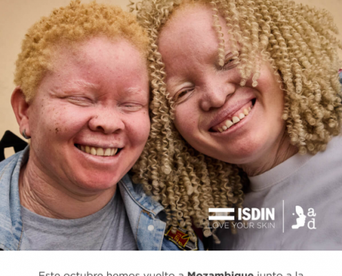 Dos personas con cabello rubio rizado posan juntas, mostrando cercanía. Texto sobre la imagen: “Desafiando el cáncer de piel”. Logotipos de ISDIN y Fundación África Directo. Texto inferior: “Este octubre hemos vuelto a Mozambique junto a la Fundación África Directo… Una nueva oportunidad para desafiar el cáncer de piel y seguir sumando resultados que marcan la diferencia”.